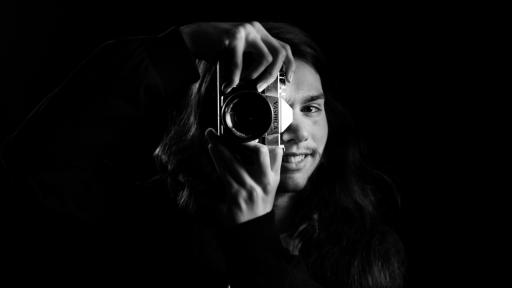 moody black and white portrait of a person smiling behind a camera lens