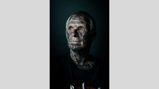 Black and white shot of man with tattoos covering much of his face and neck.