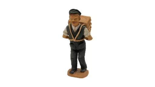 Clay sculpture of a man wearing a work uniform including a white shirt, dark grey vest, pants, boots and cap. A large case is suspended on his back with cords attached to the case strapped across his chest and his arms bent back to support the weight.