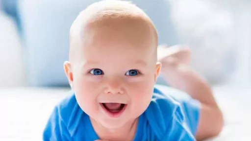 Smiling baby with blue eyes and blue clothing, lying on the stomach.