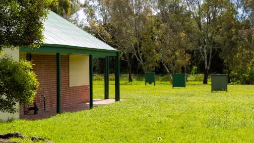 Grass area with part of a small building visible to the left. There are 3 archery targets in the distance.