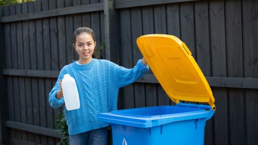 A young person standing next to an open recycling bin holding an empty milk jug