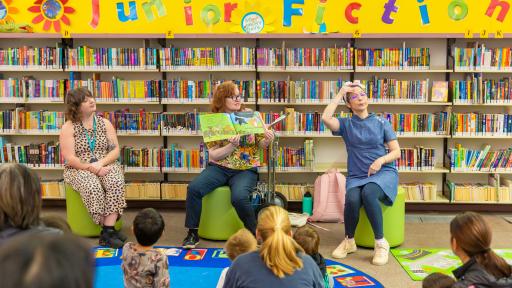 3 people in a library read a picture book and use sign language to an audience