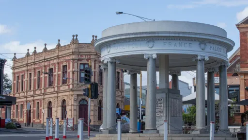 Street view of a cenotaph building on the edge of a roundabout with a historic building in background