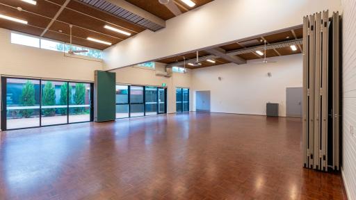 A large empty room with wooden floors and large windows looking into an outside courtyard