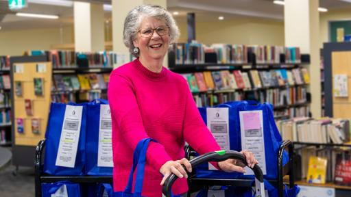 Volunteer Elizabeth Smith pushing trolley among library shelves.