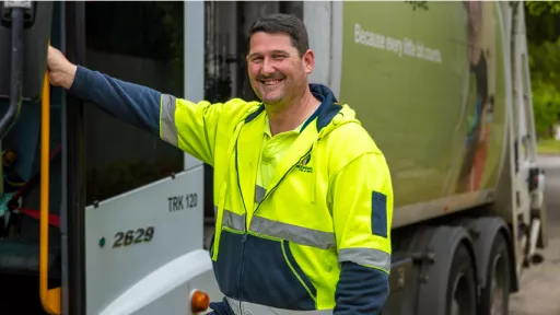 Waste truck driver in hi-vis shirt standing beside truck.