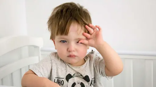 A toddler rubbing their eyes looking tired while standing in a cot