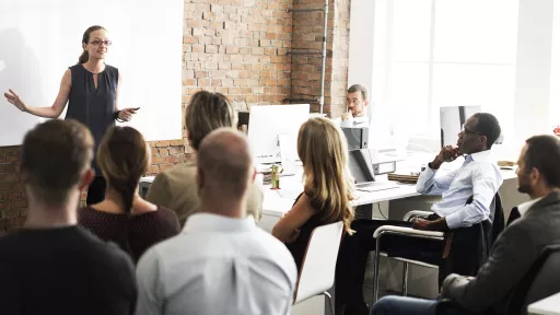 a woman lectures at a whiteboard before a room of adult students