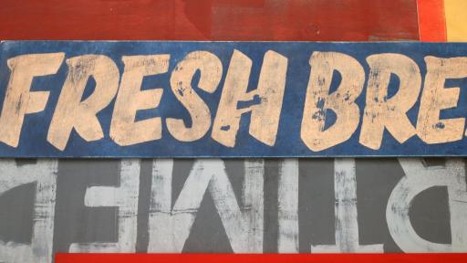 Image of two rectangular signs, one navy, the other dark grey with big letters. Above and below are other sections of signs painted in hues of red with no visible text on them. The Navy sign says ‘Fresh bre’ in capitalised, light orange painted letters. The dark grey sign is upside down with light grey letters. The letters are partially obscured, but the displayed word has a B, M, E, and R that are legible.