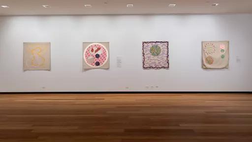 Four colorful abstract paintings hang on a white wall in an art gallery.