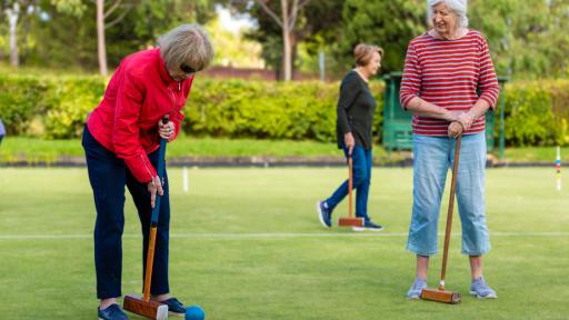 Several players on croquet green with one about to hit blue ball with mallet.
