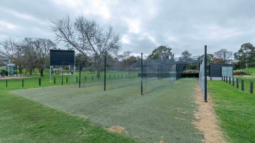 4 cricket net lanes surrounded by green grass. A score board is in the background. 