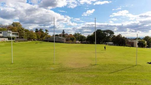 A green sports oval looking directly at 4 AFL goal posts. Trees line the edge of the oval.