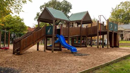 A wooden playground on a mulch surface. The playground ahs a slide and a ramp.