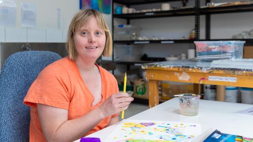 Artist Tara Wood wearing a bright orange tshirt. She is holding a yellow pencil over a drawing of butterflies.