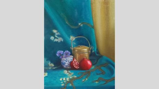 A still-life painting of a collection of objects on a draped blue and gold scarf with painted blossom trees. From left to right, the objects are a small, white ceramic cup with blue flowers painted on and small purple flowers sitting in it, a golden container with a handle, and one and a half pomegranates. 