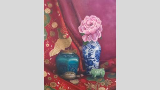 A still-life painting of a collection of objects on two draped scarves, one red with green and gold flowers and the other pink. From left to right, the objects are a blue vessel with a wooden lid and embossed flowers, a small brass decorative container with a lid, a tall white ceramic vase with blue flowers painted on and a single pink flower sitting in it, and a small jade sculpture of a pig.