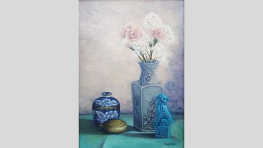 A still-life painting of a collection of objects on a green surface before a white wall. From left to right, the objects are a small blue decorative container with gold detailing and white flowers, a small round golden container with lid, a pail blue vase embossed with flowers and a bouquet of pink and white flowers sitting in it, and a small blue sculpture of a dog.