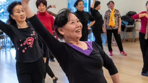 Women standing in a dancing-like pose with one arm above their head in an activities room