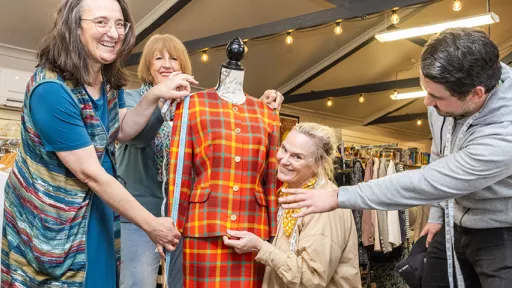 Four op shop volunteers holding measuring tapes stand with dressmaker dummy wearing brightly coloured checked suit.