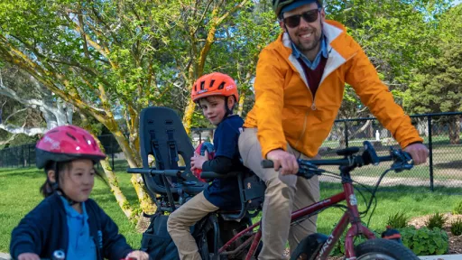 Man on electric cargo bike on shared path with child on seat, pedestrian and small child on bike