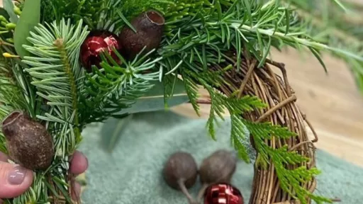 A hand is holding a wreath which is being made of green foliage and gumnuts 