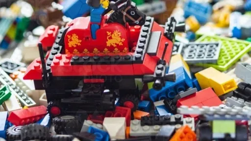a tank made out of lego being driven by a mini fig over a pile of loose lego pieces