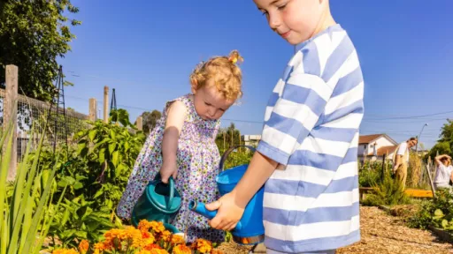 Two children water plants in community garden
