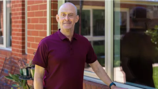 Man stands smiling next to windows outside home