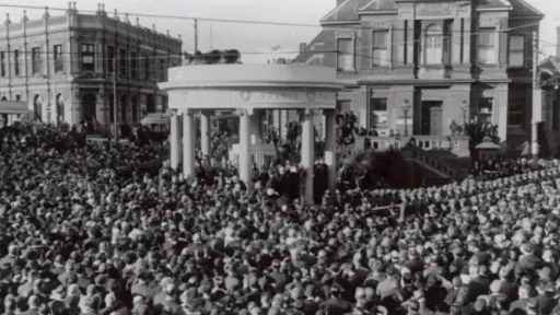 Black and white historical photo shows circular memorial surrounded by crowds of people