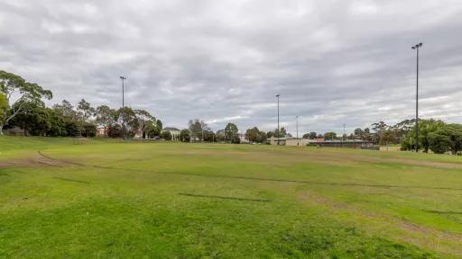 A circular sportsground. A building and another field is in the background.