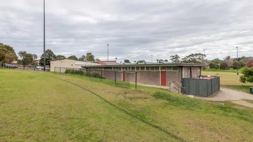 The edge of a sportsground oval looking forwards a small building