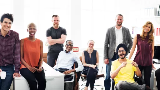 a diverse group of people sitting and standing at desks