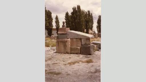 A pile of stones with a bronze bust on top, sit in a field.