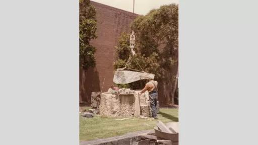 Two figures position large stones with the assistance of a crane.