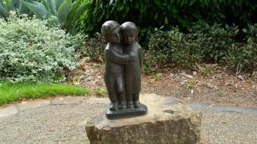 Full length bronze sculpture of a small girl and boy embracing on bronze base. The sculpture is located in a garden