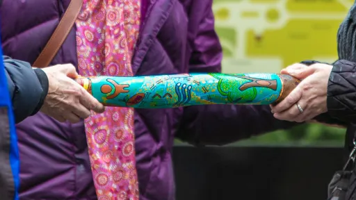 Two people holding a thick stick covered in illustrations