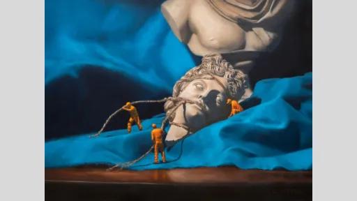 A hyper realistic painting showing a broken classical marble statue of Apollo resting on bright blue drapery. The head lies detached in the foreground, with three miniature figures in orange hazmat suits pulling ropes around it as if recovering an artifact.