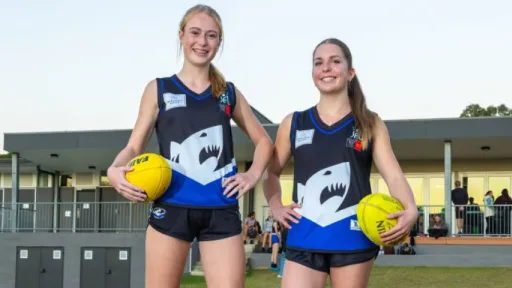 Two teenage girls in blue and black football uniforms stand smiling outside pavilion.