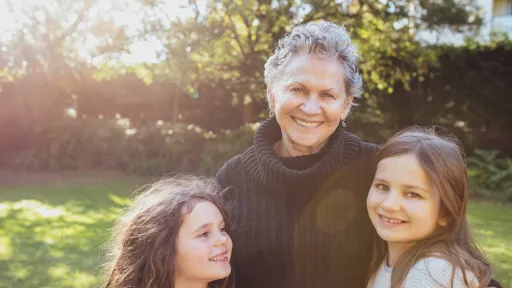 A friendly-looking older woman with her arms around 2 young girls in a garden