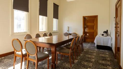 A meeting room with a large table with 12 chairs. A table with a kettle and cups is in the back corner.