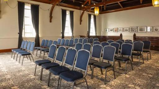 Interior of a room with rows of blue chairs facing forward. The room features patterned carpet and decorative ceiling.