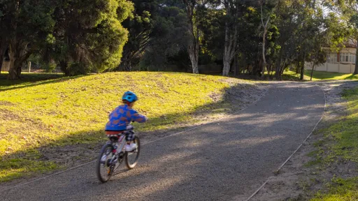 Small child rides bike on wide path with grass and trees on both sides