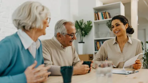 two older adults sitting at a table with a younger person who is referencing papers.