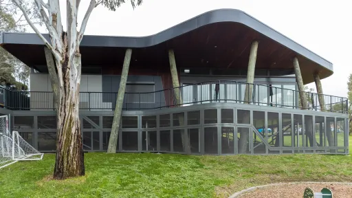 Outdoor pavilion in a park setting, with big glass windows and surrounded by green grass.