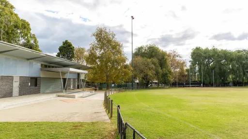 A AFL field, surrounded by a fence. A building with a sheltered area is to the left.