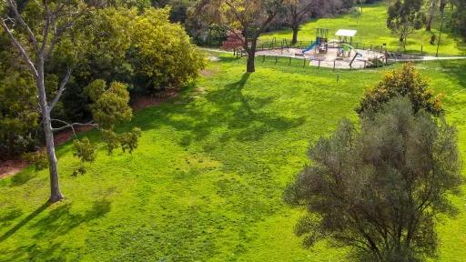 Aerial view of a large grassy area with trees. A fenced in playground is visible in the background.