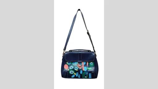 A blue bag with a shoulder strap. Body of bag is painted with graphic shapes in pink, green, white, blue and yellow. 