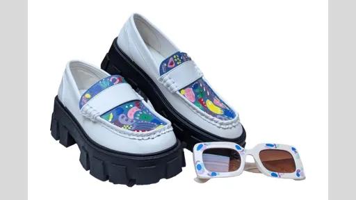 A pair of white loafers on the left and a pair of cream sunglasses on the right. Top of shoes are painted in blue, along with graphic shapes in yellow, purple, pink, and white. Sunglasses frames are painted with purple and blue graphic shapes. 